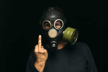 Man in gas mask shows middle fingers sign on dark background