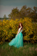 beautiful young girl with red hair in a lavish dress walking in the nature with flowers