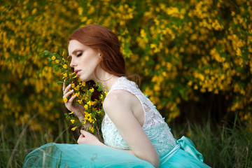 Naklejka na ściany i meble beautiful young girl with red hair in a lavish dress walking in the nature with flowers