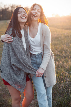 Two cute girls hugging and laughing outdoors at sunset. Best friends