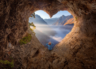 Woman in heart shape cave watching the misty canyon at morning