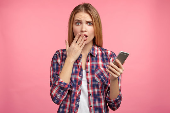 Shocked Female Model Holds Modern Mobile Phone, Missed Important Call From Partner, Being Puzzled. Horrified Woman Looks At Electronic Watch On Smart Phone, Realizes That She Is Late On Meeting