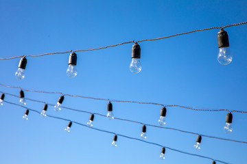 Vintage antique hanging light bulbs at the blue sky. Holidays and business good idea concept.