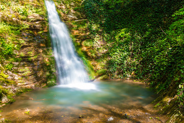 Long exposure photo of the waterfall and little lake in the park Berendeyevo Tsarstvo in sunny summer day, Sochi, Russia