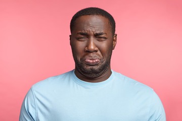 Black man has sorrorful miserable expression being depressed after fired on work, cries, has stressful situation, dressed casually, isolated over pink background. Plump unshaven African man in panic