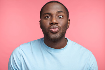 Pleasant looking African American man rounds lips, going to recieve kiss from beautiful girl, being in anticipation of pleasant moment. Attractive black man sends kiss for you. Sympathy and feelings