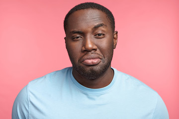 Fototapeta premium Plump dark skinned African guy raises eyebrow, has full lips, tired and sleepless expression, isolated over pink background. Black man poses in studio. People, lifestyle, expressions concept