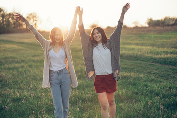 Two young women with raised hands under the sunset light