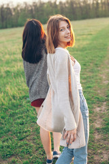 Two girls walking outdoors at sunset. One girl has turn around. Best friends