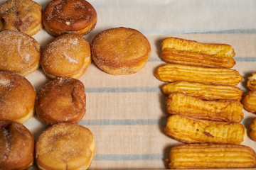 Sweet baked donuts and eclairs on a wooden tray