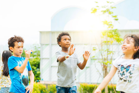 Happy little kids blowing soap bubbles in summer park. Kid and friends in international preschool play a bubble in playground with sunset background, kid, child, school, play and summer background.