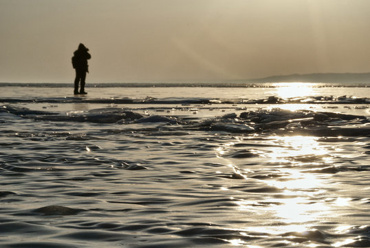 a photographer on the ice of lake Baikal makes a photo of the sunset