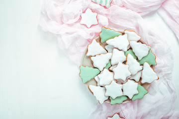 Christmas gingerbread cookies on a plate. Cookies covered with multi colored icing in pale pastel colors shaped as fir-tree and star. White background, pink napkin
