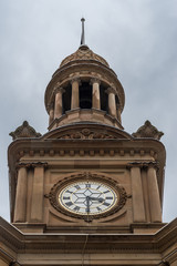 Sydney, Australia - March 25, 2017: Closeup of top of brown stone Town Hall Clock Tower. White and gold time piece. Against heavy gray sky.