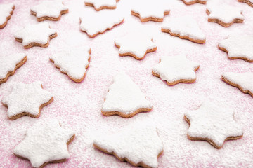 Christmas gingerbread pattern, top view, flat lay. Cookies covered with white icing and powdered sugar in pale pastel colors shaped as fir-tree and star. Pink wooden background