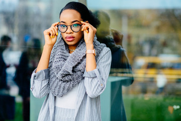 Fototapeta premium Gorgeous african business woman in glasses having cold over glass case with city reflection background.