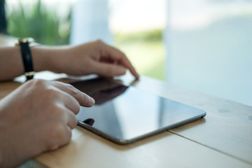Closeup image of a woman's hands pointing , touching and using tablet pc  on wooden table in cafe