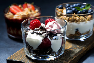 various desserts with fresh berries and cream on dark background, horizontal