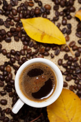 Coffee cup on sackcloth with autumn leafs and coffee beans around