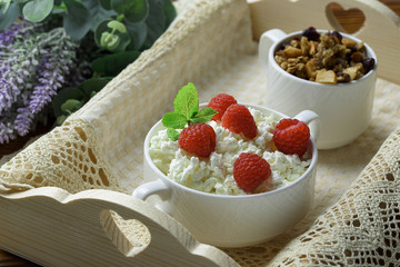 Homemade breakfast: cottage cheese with fresh raspberries and granola. In a white porcelain bowl, on a wooden tray