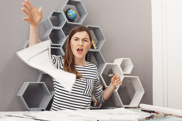 Close up portrait of young unhappy good-looking female freelance engineer throwing work papers away...