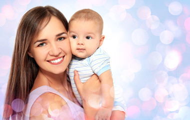 Portrait of happy young woman with cute baby on blurred lights background