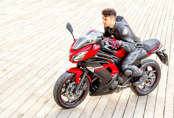 Obraz premium Handsome rider guy in black leather biker jacket ride on classic style racer motorbike.