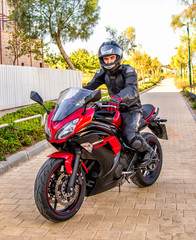 Handsome rider guy in black leather biker jacket and helmet ride on classic style racer motorbike.