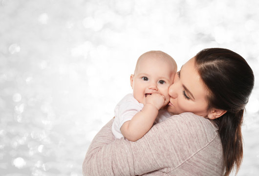 Portrait of happy young woman with cute baby on light background