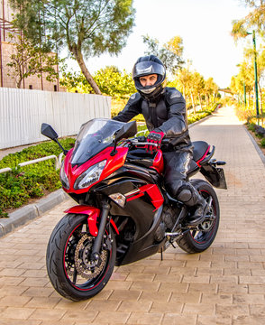 Handsome rider guy in black leather biker jacket and helmet ride on classic style racer motorbike.