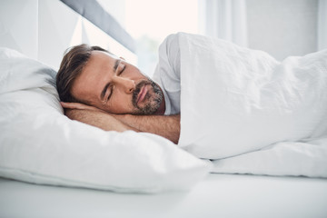 Man sleeping in bed with soft daylight. Sleep or rest concept.