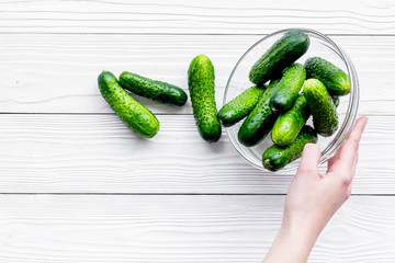 Hand takes bowl with fresh cucumbers. Grey wooden background top view copyspace
