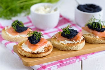 Appetizer toast bread with cream cheese, smoked salmon and black caviar decorated by dill.
