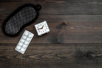 Sleeping pills for insomnia near sleep mask and alarm clock on dark wooden background top view copyspace