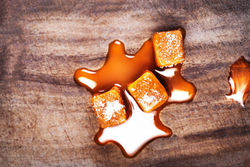 Homemade  Caramel sauce flowing on caramel candies on wooden  background. Golden Butterscotch toffee candy caramels.