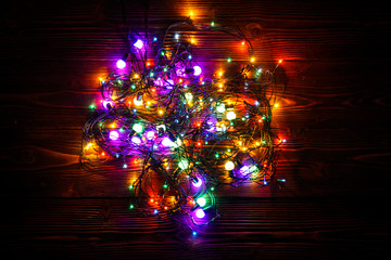 Wreath and garlands of colored light bulbs.Christmas background with lights and free text space. Christmas lights border. Glowing colorful Christmas lights on a wooden background. New Year.  