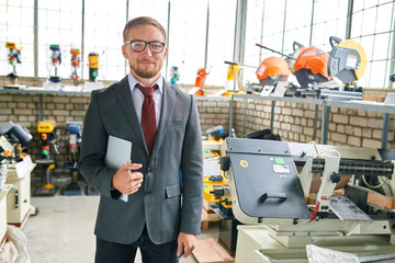 Portrait of successful salesman wearing suit posing looking at camera, standing by machine tools in...