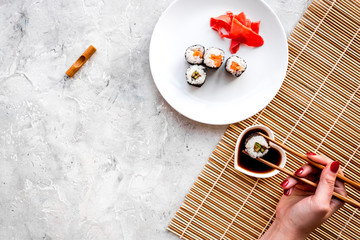 Hand takes sushi roll with salmon and avocado with chopstick. Grey stone and mat background top view copyspace