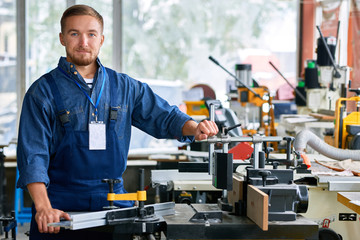 Portrait of young worker posing looking at camera with machine units in modern factory showroom , copy space