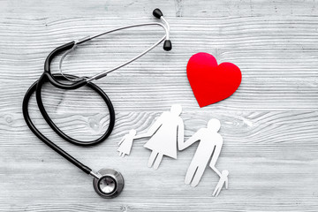 Choose health insurance. Stethoscope, paper heart and silhouette of family on grey wooden background top view