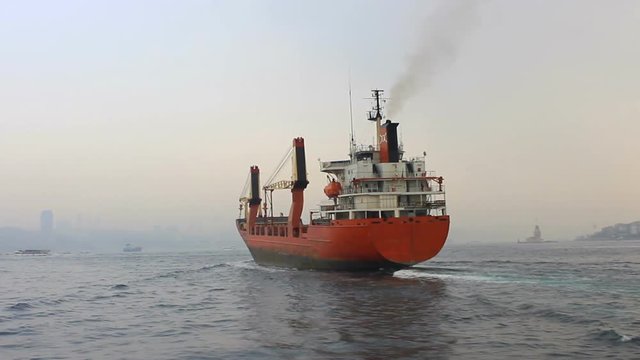 Cargo ship sailing in mist. Tracking shot of the industrial ship. Back view of the red cargo container ship. Istanbul in smog with a cargo ship pass through slowly