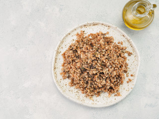 Buckwheat risotto with dried mushrooms in craft plate on light gray or white cement background. Gluten-free and vegetarian buckwheat recipe ideas. Copy space. Top view or flat-lay.