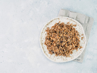 Buckwheat risotto with dried mushrooms in craft plate on light gray or white cement background. Gluten-free and vegetarian buckwheat recipe ideas. Copy space. Top view or flat-lay.