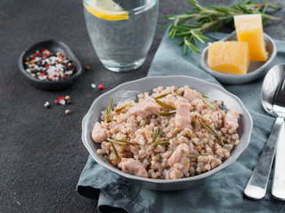 Raw buckwheat risotto with chicken meat and rosemary served parmesan cheese in gray plate on black cement background. Gluten-free and buckwheat recipe ideas. Copy space