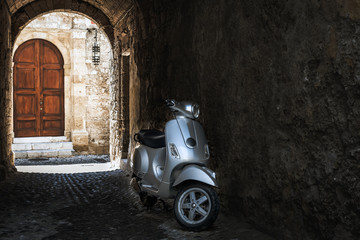 Motorbike in dark arch of Rhodes town with old wooden door on a background. Rhodes island, Greece