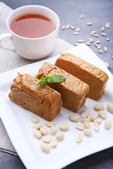 Tasty slices of halva in white plate with cup of tea on wooden table