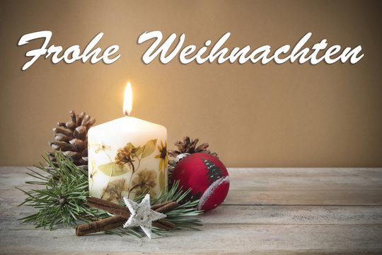 Christmas decoration with candle, pine, bauble, with text in German "Frohe Weihnachten" in wooden background