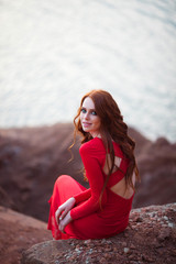 portrait of a beautiful young girl with red hair in a red tight dress near the lake shore