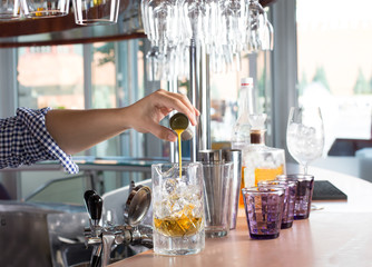 Bartender holding steel jigger and pouring orange liquor into the glass with ice.