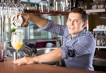 Smiling handsome bartender pouring a drink into the glass out of the steel shaker.
